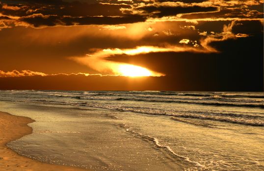 Waves roll in at dawn as the sun breaks through clouds.