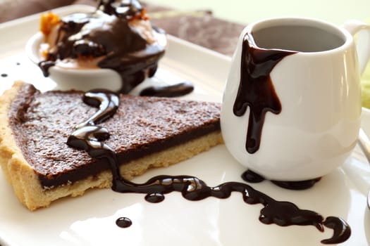 Chocolate tart slice and ice cream with melted chocolate from a jug.