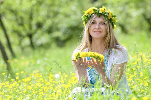woman with flower wreath siting in a spring meadow