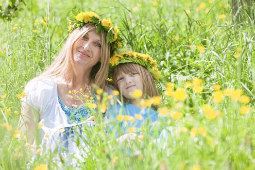 mother and son with flower wreaths sitting in a spring meadow
