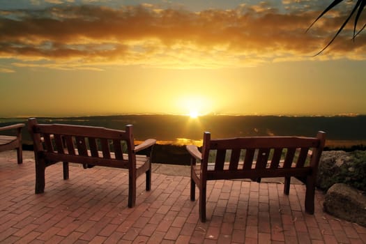 Park benches with a blazing cloudy sunrise over a view of a valley.