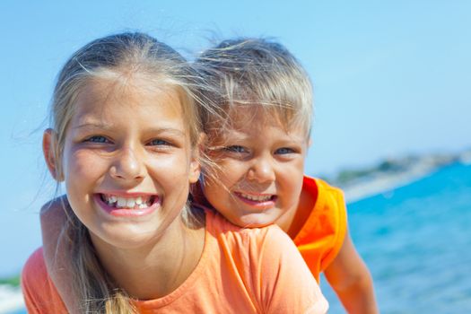 Smiling happy brother and sister posing on a beach. In the background the sea