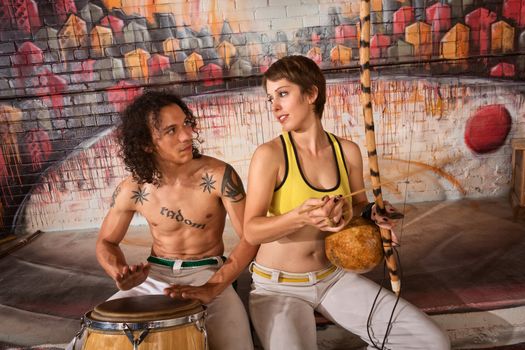 Cute young couple in capoeira outfit playing traditional instruments