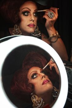 Cross dressing man putting on makeup at a mirror