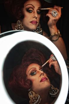 Drag queen applying makeup in front of a mirror