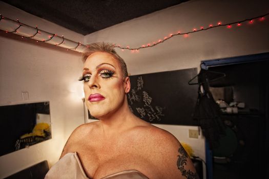 Serious drag queen with bra and tattoo in dressing room