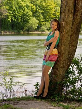 The young slender nice girl costs in a tree shadow in the sunny summer day