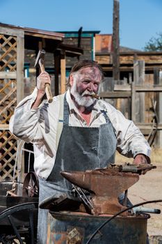 Male Blacksmith in Old West Swings Hammer at Anvil