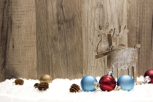 christmas decoration with wood background, snow, elk, christmas baubles gold, blue and red and pine cones