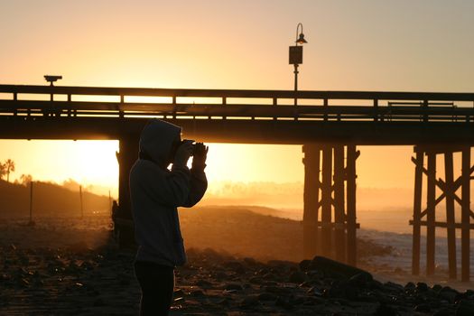 Photographer at sunset sunrise near the pier by the beach and ocean.