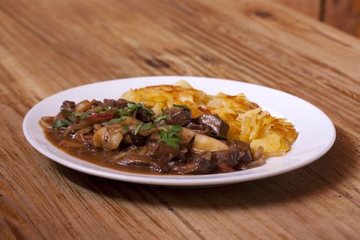 Venison goulash with apples and potatoes on plate with wooden background