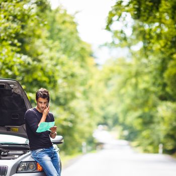 Handsome young man calling for assistance with his car broken down by the roadside