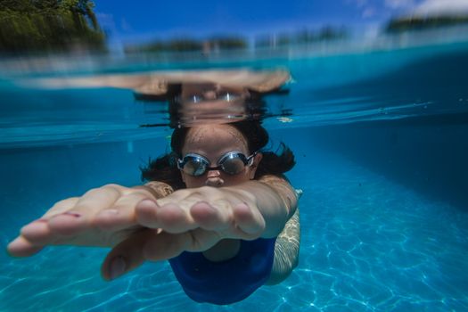 Young girl wearing training goggles swimming glide underwater close to lens.