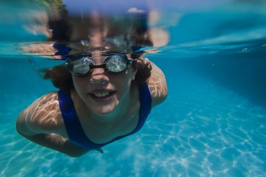 Young girl wearing training goggles swimming glide underwater close to lens.