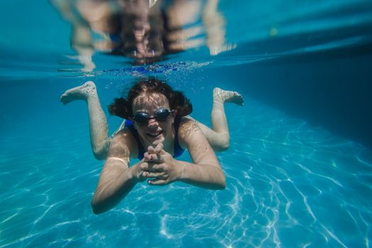 Young girl wearing training goggles swimming glide underwater close to lens.