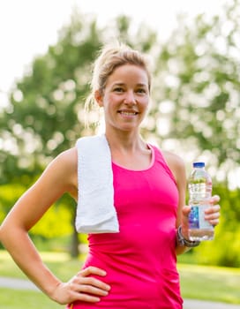 Portrait of an attractive athlete drinking water from bottle after a workout in nature
