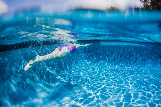 Young girl training swimming glides underwater towards distant wall.