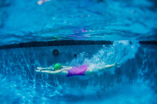 Young girl glides underwater from dive into swimming pool.