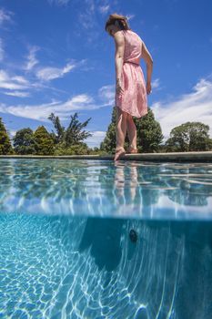Teenage girl tests water temperature of pool to swim.