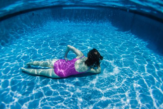 Young girl in summer fun play mode poses underwater in swimming pool