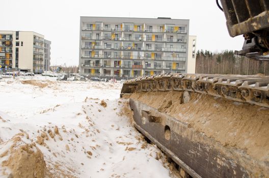 heavy machinery tractor caterpillar and cars stand near new modern apaprtment house. winter snow.