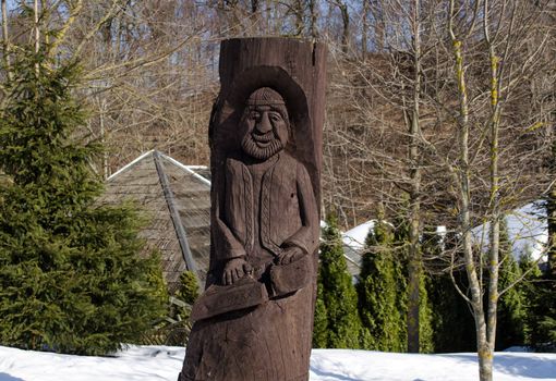 rural grunge wooden carved man statue surrounded by snow in winter park.