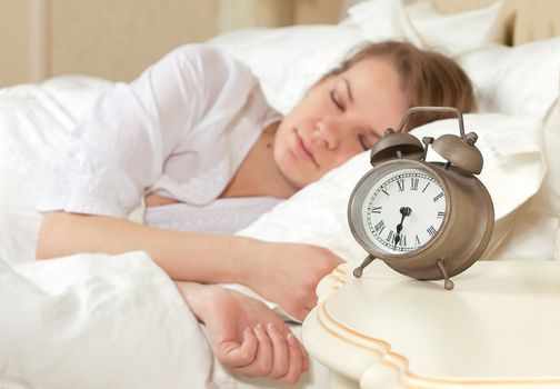 Beautiful sleeping woman resting in bed with alarm clock ready to wake her in the morning.