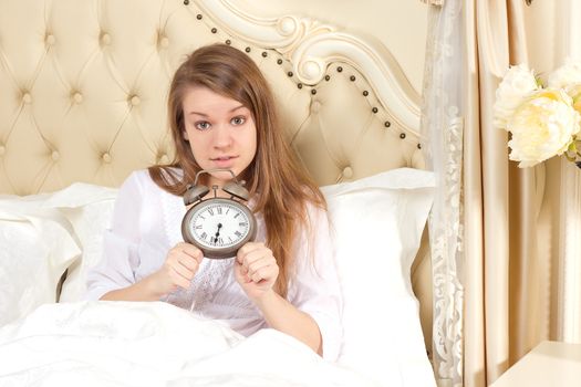 Young woman with alarmclock on the bed at the morning