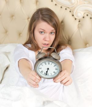 Young woman with alarmclock on the bed at the morning