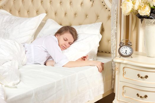 Beautiful sleeping woman resting in bed with alarm clock ready to wake her in the morning.