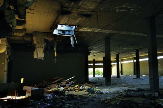 Abandoned factory interior tattered insulation material hanging from the ceiling.