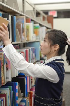 Smart female student picking and taking a book from a library shelf