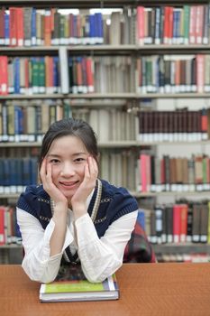 Portrait of young female student on sitting at a desk in front of a library shelf