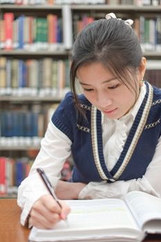 Portrait of young female student doing home work in front of library bookshelf