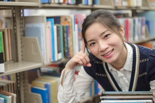 Portrait of young student holding a stack of text books near a library bookshelf