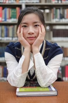 Portrait of young female student on sitting at a desk in front of a library shelf