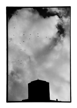 Church silhouette under cloudy sky and flock of flying birds. Old black and white photo darkroom print with dust and scratches, Meteora, Greece circa 1990.