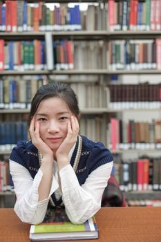 Portrait of young female student on sitting at a desk in front of a library shelf