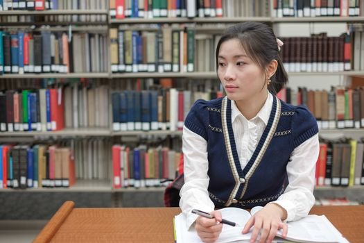 Portrait of young female student on sitting at a desk in front of a library shelf