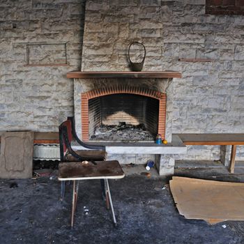 Chair and table close to dirty fireplace. Abandoned decayed house interior.