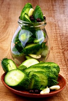 Arrangement of Sliced Delicious Pickled Cucumbers in Brown Plate and Glass Jar closeup on Wooden background