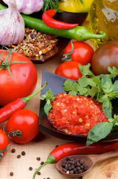 Arrangement of Bruschetta Sauce in Black Bowl with Tomatoes, Greens, Spices, Garlic and Black Peppercorn in Wooden Spoon closeup on Wooden background