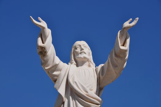 Jesus Christ with hands raised in blessing under blue sky. Marble funerary statue.