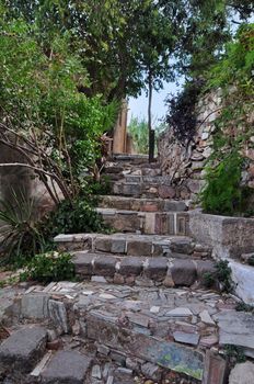 Stone steps decorated with ancient Greek symbols. Picturesque narrow street below the Acropolis rock in Plaka, Athens Greece.