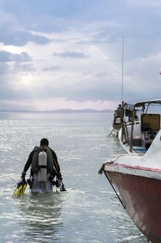 A diver walking towards the ocean with some empty boats beside him.
