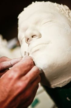 Artist sculpting a realistic male human face from clay, closeup view of the artists hands