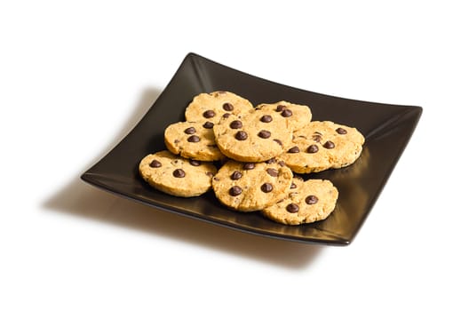 Pile of chocolate chip cookies on a square black plate, isolated on white background