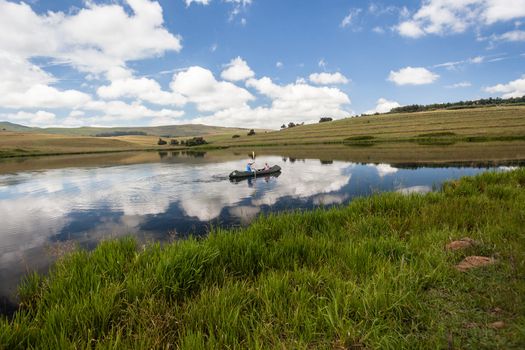 Boy girl canoeing with blue sky and clouds reflections on smooth mirror dam waters.