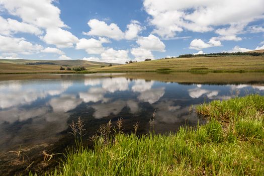 Summer mountain lake dam with still glass smooth waters reflecting  blue sky clouds .