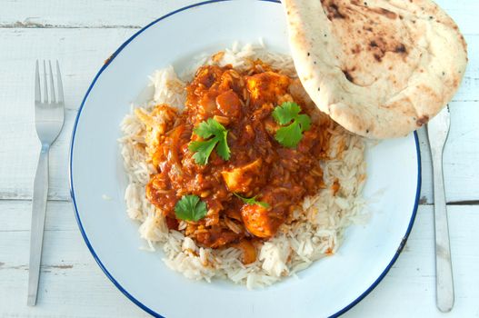 Plate of chicken curry with coriander and naan bread on the side 